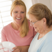 Smiling Senior Adult Woman and Young Daughter Talking At Sink in Kitchen. Betreuungskraft – Aufgaben, Leistungen & Alltag