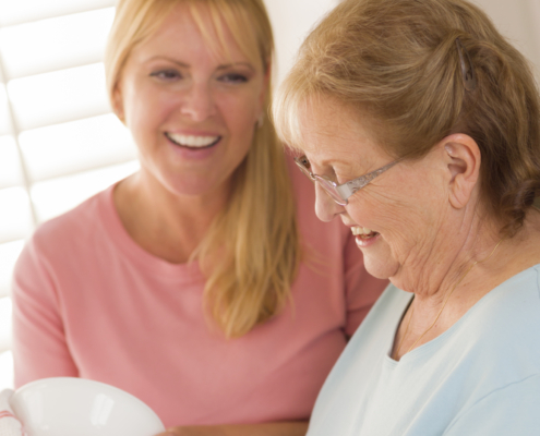 Smiling Senior Adult Woman and Young Daughter Talking At Sink in Kitchen. Betreuungskraft – Aufgaben, Leistungen & Alltag